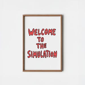 May include: A rectangular wooden frame containing a white print with the red text "WELCOME TO THE SIMULATION" written in a bold, rounded, hand-drawn style font. The frame has a natural brown finish and surrounds the centered text on a white background.