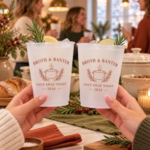 Op de afbeelding: Twee matglazen kunststof bekers met de rode tekst BROTH & BANTER, SOUP SWAP NIGHT en 2026, en een afbeelding van een kookpan. Elke beker bevat ijs, een schijfje citroen en een takje rozemarijn, vastgehouden voor een wazige achtergrond.