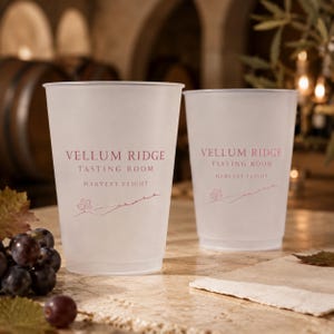 May include: Two translucent frosted plastic cups featuring the red printed text Vellum Ridge Tasting Room Harvest Flight and a small line drawing of a grape leaf. The cups have a tapered cylindrical shape with a smooth rim and base.