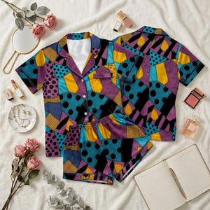 May include: A short-sleeve button-down pajama shirt and matching shorts set featuring a patchwork pattern of purple, yellow, and teal blue sections with black polka dots, solid black shapes, and cross-hatched grid textures throughout the fabric.