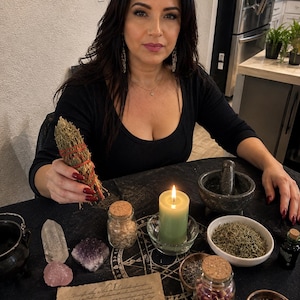 Puede incluir: Un manojo de hierbas secas atado con hilo rojo, una vela verde en un portavelas de cristal, un mortero de piedra, cristales transparentes y amatista, cuarzo rosa, frascos de vidrio con corcho y un pequeño cuchillo sobre papel pergamino.