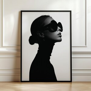 May include: A black and white framed wall art print featuring a high-contrast silhouette of a person in profile. The subject wears large, dark, rounded sunglasses and a high-neck garment, with their hair pulled back into a neat, low bun.