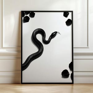 Könnte beinhalten: Ein gerahmter Wandkunstdruck, der eine glänzend schwarze Schlange mit sichtbarer Zunge auf einem rein weißen Hintergrund zeigt. Mehrere kleine, dunkle, unregelmäßige Formen sind in der Nähe der Ecken des Rahmens verstreut.