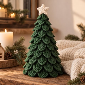 May include: A decorative tabletop Christmas tree crafted from dark green yarn with a layered, scale-like texture. The tree is topped with a small, cream-colored crocheted star. The structure is conical, featuring individual leaf-shaped segments.