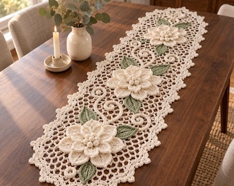 May include: A cream-colored crocheted table runner featuring three large, dimensional floral motifs with layered petals and small central spheres. The runner includes sage green crocheted leaves and intricate scrollwork, finished with a scalloped edge.