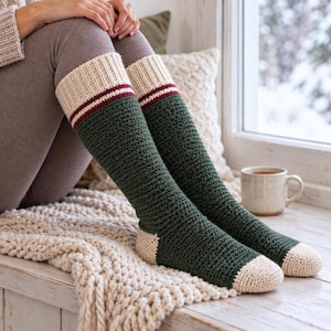 Pode incluir: Um par de meias de crochê até o joelho com corpo verde floresta escuro, pontas e calcanhares cor de creme e um punho canelado creme acentuado com uma fina listra bordô. As meias são feitas com um padrão de ponto texturizado na perna.