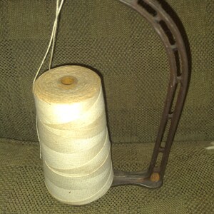 May include: A vintage metal thread holder with a spool of white thread. The holder has a curved arm and a base with a decorative design.