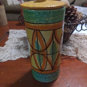 May include: A ceramic jar with a yellow lid and a geometric design in shades of green, orange, and yellow.