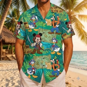 May include: A short-sleeve button-down shirt featuring a green tropical leaf background with a repeating pattern of Disney characters dressed as pirates, including Mickey Mouse, Donald Duck, and Goofy, alongside treasure chests and maps.