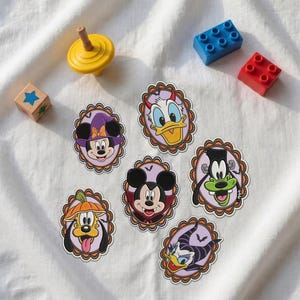 May include: Six oval stickers featuring Disney characters in Halloween costumes: Minnie Mouse as a witch, Donald Duck as a devil, Goofy as Frankenstein's monster, Pluto as a pumpkin, Mickey Mouse as a vampire, and Daisy Duck as Maleficent.