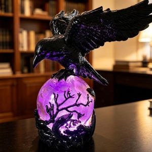 May include: A black raven sculpture with wings spread wide, perched atop a glowing purple orb. The orb features a dark, intricate silhouette of bare tree branches and a dragon-like creature, creating a vibrant contrast against the dark bird.