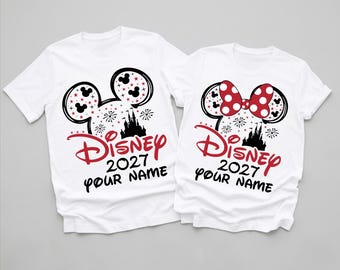May include: Two white short-sleeve t-shirts featuring a graphic of a Mickey Mouse ear silhouette filled with stars and a castle. The design includes the red text Disney 2027 and the black text YOUR NAME. One shirt features a red polka dot bow.