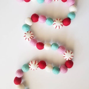 May include: A festive garland made of felt balls in red, pink, white, and turquoise colors. The garland features peppermint candy designs.