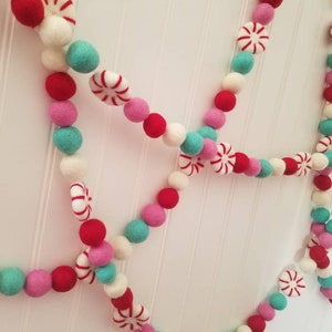 May include: A festive garland made of felt balls in red, pink, white, and turquoise with peppermint candy decorations.