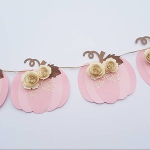 May include: A pink and brown paper pumpkin garland with white paper flowers. The garland is strung together with twine.
