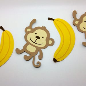 May include: Three paper cutouts of monkeys and bananas. The monkeys are brown with yellow faces and black eyes. The bananas are yellow.
