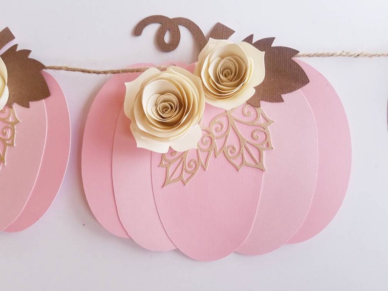 May include: A pink paper pumpkin garland with brown leaves and cream paper roses. The garland is strung with twine.