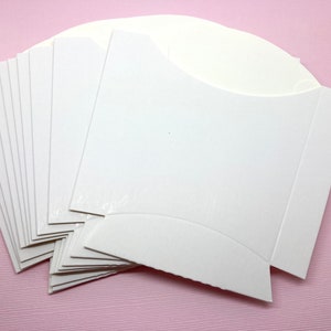 May include: A stack of ten white cardboard favor boxes with a curved top and a fold-over flap.