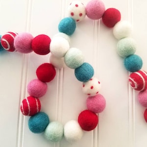 May include: A garland of felt balls in red, pink, white, and teal. The balls have different patterns, including polka dots and stripes.