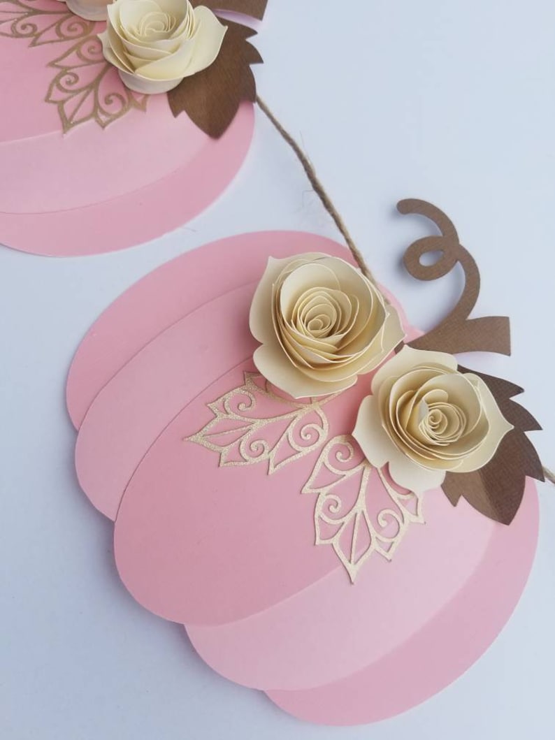 May include: A pink paper pumpkin garland with brown paper leaves and cream paper flowers. The garland is strung together with twine.