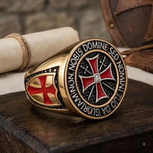 Può includere: Un anello color oro con una faccia circolare caratterizzata da una croce smaltata rossa, una pietra centrale trasparente e l'iscrizione latina NON NOBIS DOMINE SED NOMINI TUO DA GLORIAM. Il lato dell'anello mostra uno scudo con croce rossa.