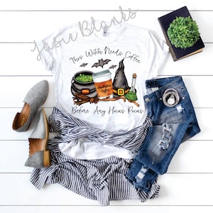 May include: White t-shirt with a Halloween-themed graphic. The design includes a witch's cauldron, coffee cup, witch hat, and potion bottle. Text reads "This Witch Needs Coffee Before Any Hocus Pocus".