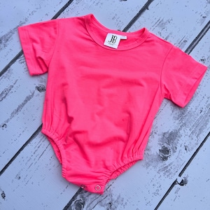 May include: A bright pink short-sleeved bodysuit with a white tag that says "JB" on it.