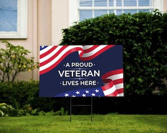 May include: A blue and white yard sign with a red, white, and blue American flag design. The sign reads "A Proud Veteran Lives Here."