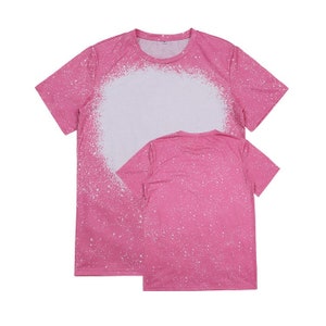 May include: Two pink t-shirts with a white splatter paint design. The front of the top shirt has a large white circle in the center.