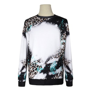 May include: A white sweatshirt with a black and brown leopard print design. The print has a faded, spray-painted effect with turquoise accents.
