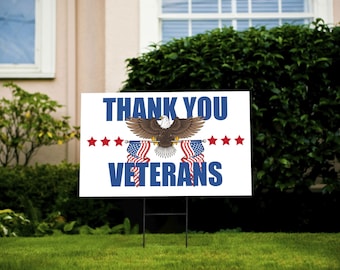 May include: A white sign with blue and red text that reads "Thank You Veterans". The sign features an American bald eagle holding two American flags in its talons. There are five red stars on each side of the eagle.