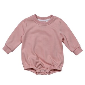 May include: A pink long-sleeved baby onesie with a round neckline and snap closures at the bottom.