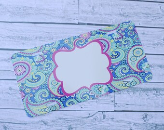 May include: A blue, green, and pink patterned license plate with a white blank space in the center. The license plate has a pink border around the blank space.
