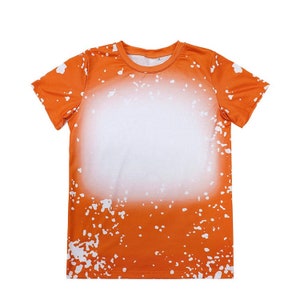 May include: Orange short-sleeved t-shirt with a white splatter paint design. The shirt has a crew neck and a relaxed fit.