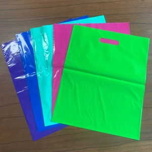 May include: Five plastic shopping bags in different colors: blue, turquoise, pink, and green. The green bag has a handle.