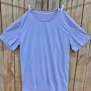 May include: A plain, light purple t-shirt hanging on a clothesline with white clothespins.