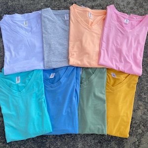 May include: Eight V-neck t-shirts in various colors, including white, gray, peach, pink, turquoise, blue, green, and yellow. Each shirt has a small tag with the letters "JB" on it.