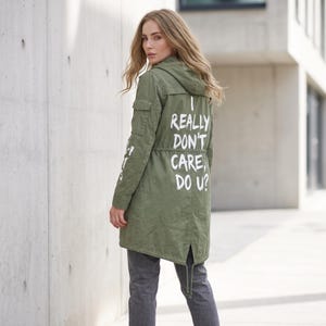 Può includere: Una giacca utility con cappuccio color verde oliva con la scritta bianca sul retro I REALLY DON'T CARE, DO U? La giacca presenta un cordoncino in vita, un orlo a coda di pesce e una tasca con patta sulla manica, abbinata a pantaloni grigio scuro.
