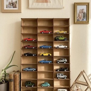 May include: A tall, rectangular wooden display shelf with three vertical columns and multiple horizontal tiers, containing a collection of various miniature toy cars, including sedans, sports cars, SUVs, and a van, arranged across the open compartments.