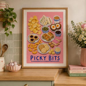 May include: A framed art print on a pink background featuring illustrations of various snacks including potato chips, sandwiches, scotch eggs, and pastries, with the text "PICKY BITS" printed in blue at the bottom of the composition.
