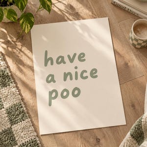 May include: A rectangular white poster featuring the sage green text "have a nice poo" in a rounded, lowercase sans-serif font. The print is positioned vertically, displaying clear, bold lettering centered on the smooth, matte surface of the paper.