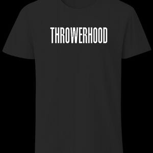 Puede incluir: Una camiseta negra de manga corta con la palabra THROWERHOOD impresa en letras mayúsculas blancas en el centro del pecho. La prenda tiene un cuello redondo y un corte estándar, mostrando un diseño limpio y sencillo sobre tela oscura.