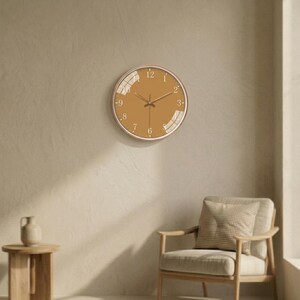 May include: A circular wall clock featuring a solid ochre-colored face with white numerical hour markers and thin, matching white hour, minute, and second hands. The clock is encased in a thin, light-toned frame and has a smooth, reflective surface.