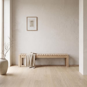 Puede incluir: Un banco de madera de color claro con un diseño de asiento de listones. Una manta de tela beige está colocada sobre un lado del banco. El banco cuenta con cuatro patas resistentes y un marco horizontal, ofreciendo una estructura simple para sentarse.