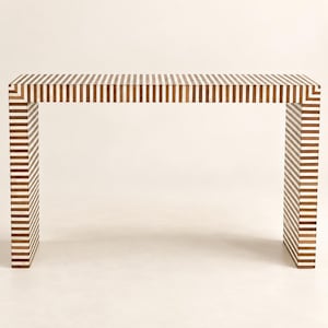 Può includere: Un tavolo console rettangolare caratterizzato da un motivo ripetitivo di strisce verticali alternate color marrone scuro e bianco sporco. Il tavolo presenta un piano d'appoggio piatto e due pannelli laterali che arrivano a terra.