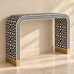 May include: A waterfall console table featuring a black and white geometric star pattern across its entire surface. The table has a continuous curved frame with a border of small black and white squares and solid gold-toned metal feet at the base.