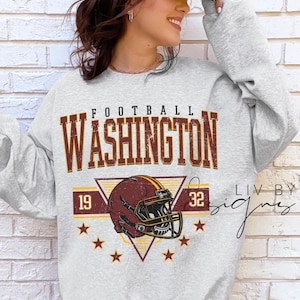 May include: A light grey crewneck sweatshirt featuring a distressed graphic print with the text FOOTBALL WASHINGTON, the numbers 19 and 32, a burgundy and gold football helmet, and six small stars arranged in a triangular pattern.