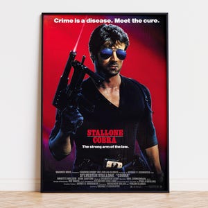 May include: A film poster for Cobra featuring Sylvester Stallone in a black shirt and blue-tinted sunglasses, holding a submachine gun with a laser sight. The background is red with the text Crime is a disease. Meet the cure. and The strong arm of the law.