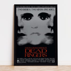 May include: A framed movie poster for Dead Ringers featuring a black and white graphic of two faces merged together. The text reads: FROM THE DIRECTOR OF THE FLY COMES A NEW KIND OF THRILLER. TWO BODIES. TWO MINDS. ONE SOUL. DAVID CRONENBERG'S DEAD RINGERS.