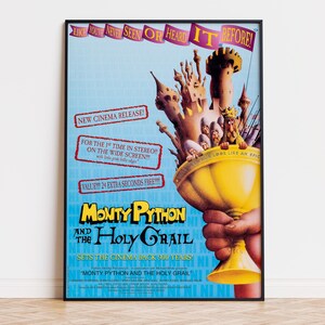 May include: A framed movie poster for Monty Python and the Holy Grail featuring a large yellow chalice held by a hand, with a castle and knights emerging from the top. The light blue background includes red text boxes and the title in black lettering.